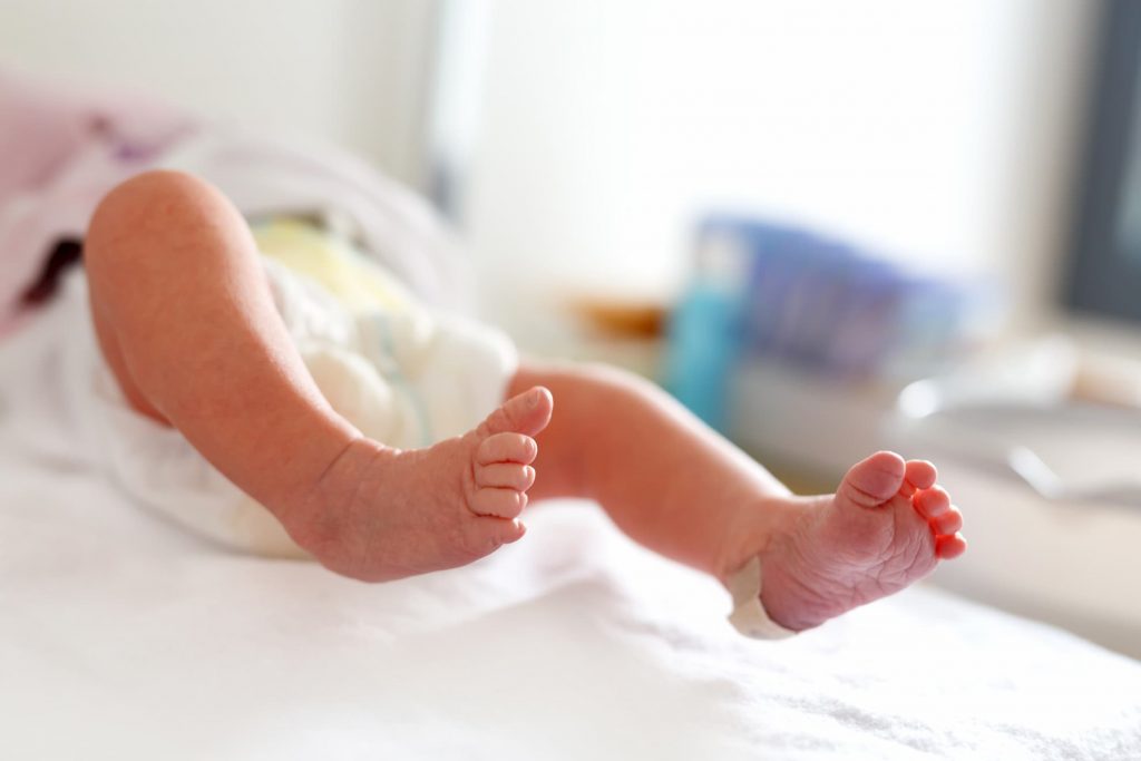 Feet of Newborn child seconds and minutes after birth. Cute tiny new born baby girl on towel with visitor information for visiting family birthing