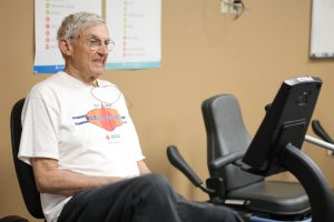 Older man experiencing cardiac rehab services by riding on stationay bike/elliptical