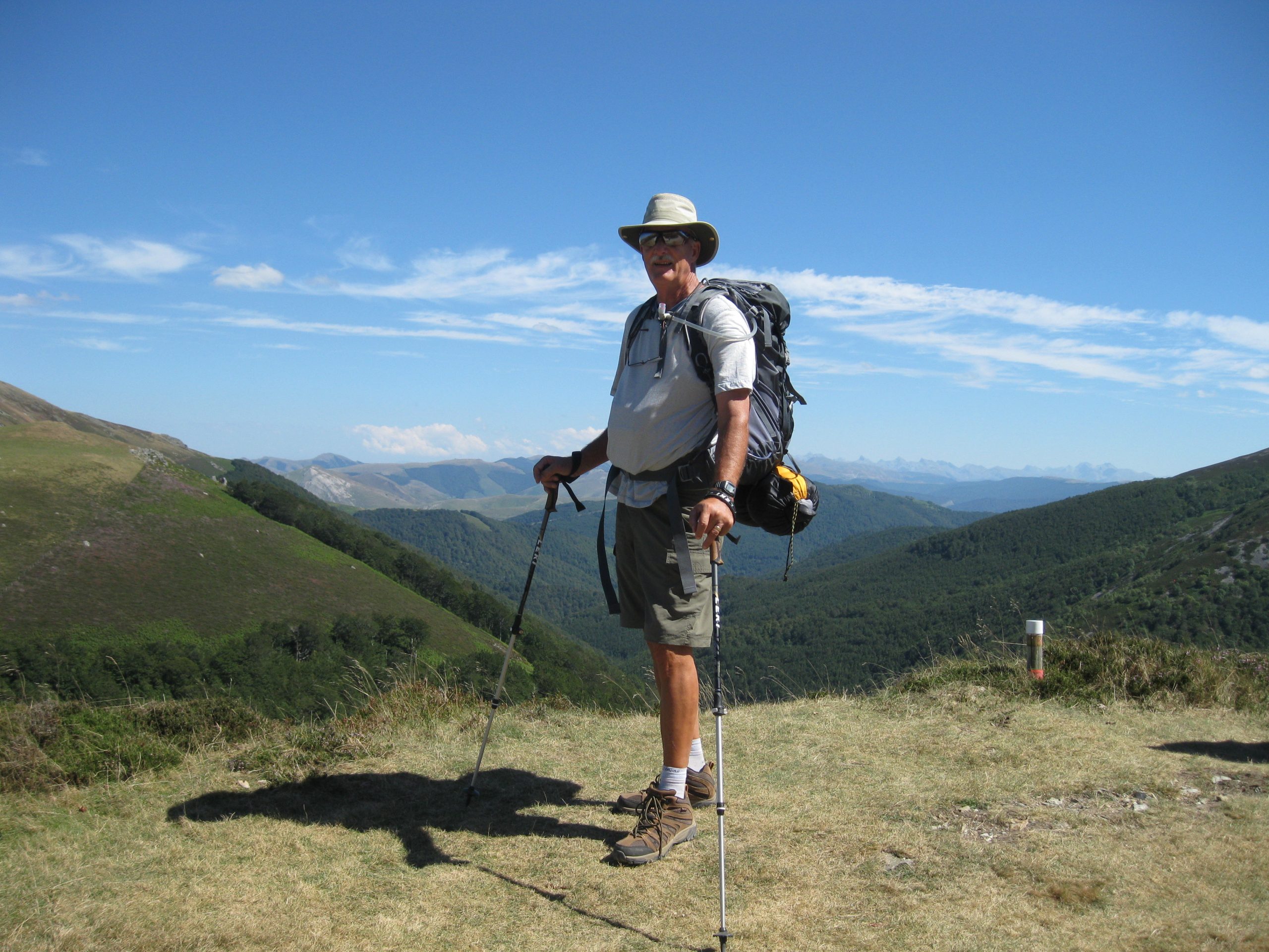 Man with backpack and walking sticks standing on top of a mountain