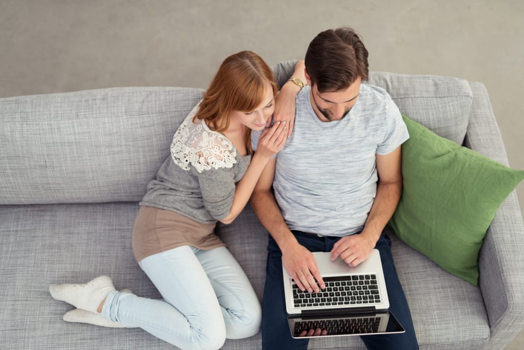 Young couple relaxing together on a large comfortable sofa with a laptop computer surfing the internet, view from above