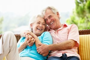 Old couple holding each other, sitting outside on patio smiling and laughing together