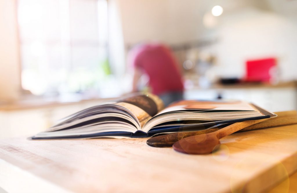 Cook book laid on a kitchen table with two wooden spoons