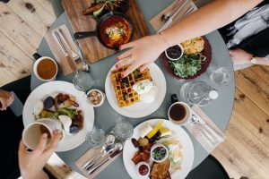 table full of breakfast items like waffles, coffee, omelets and sausage with two hands reaching across plates