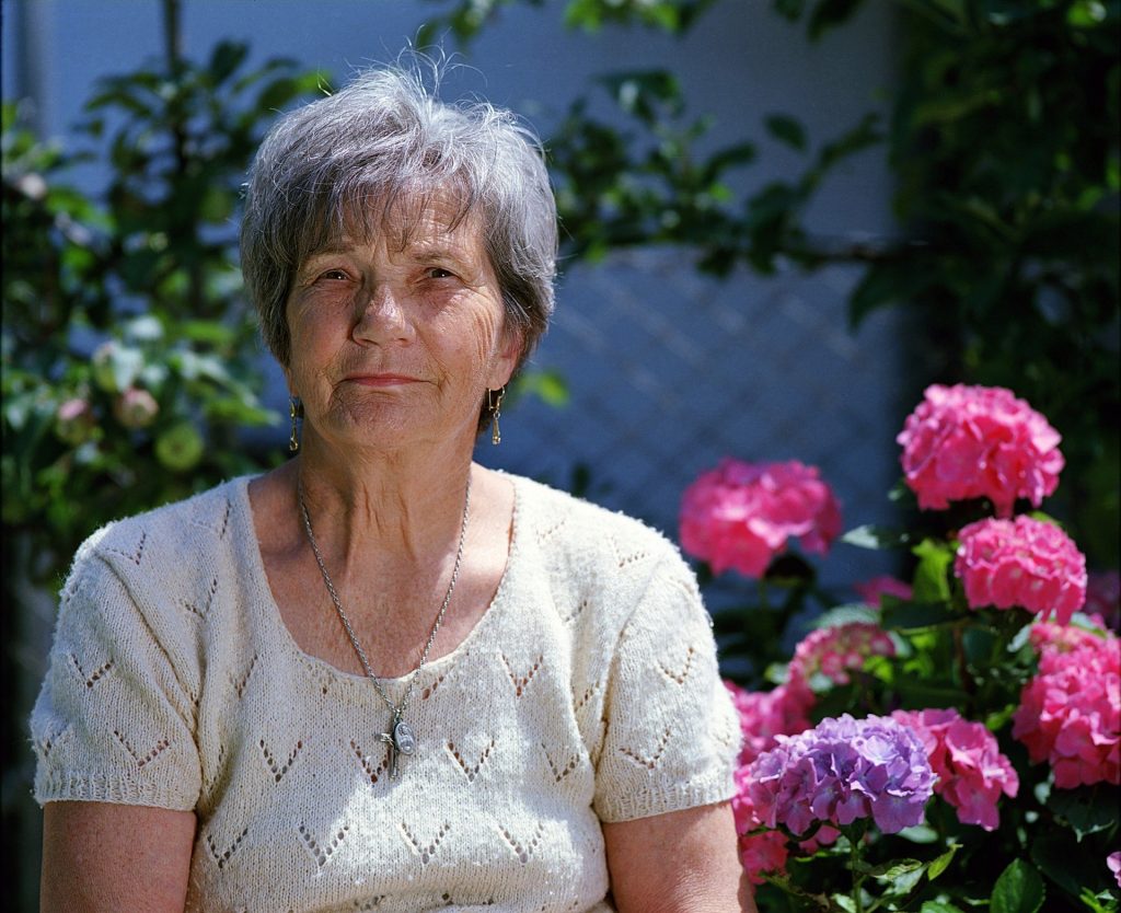 Elderly woman looking at camera with pink carnations in the background