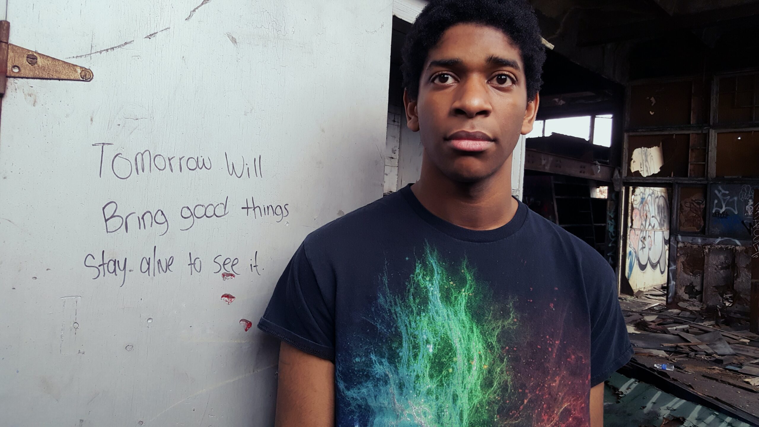 black teen standing against wall with suicide awareness message written on it