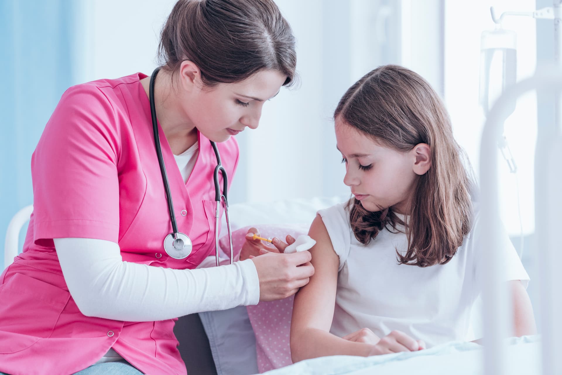 Pediatric nurse in pink scrubs giving flu shot to older girl child