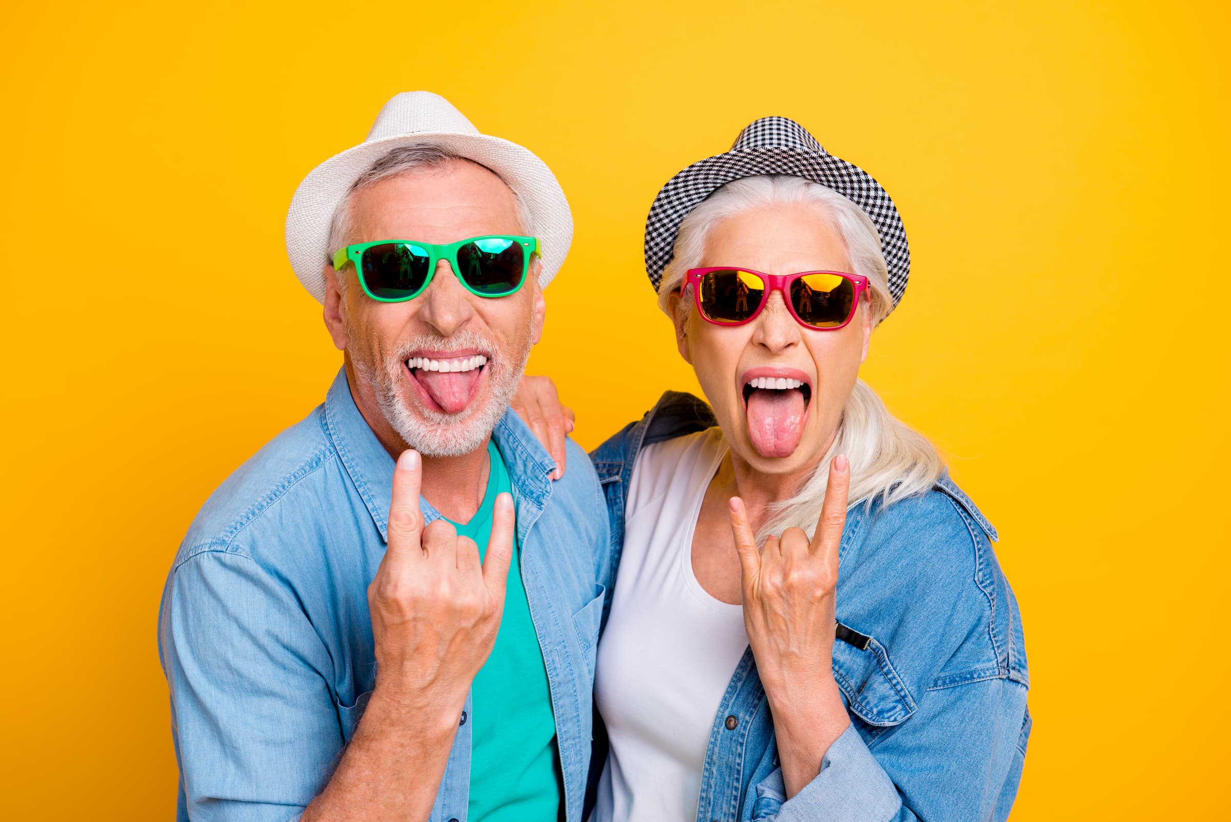 elderly white man and elderly white woman sticking out tongue and holding up "rock" on symbol