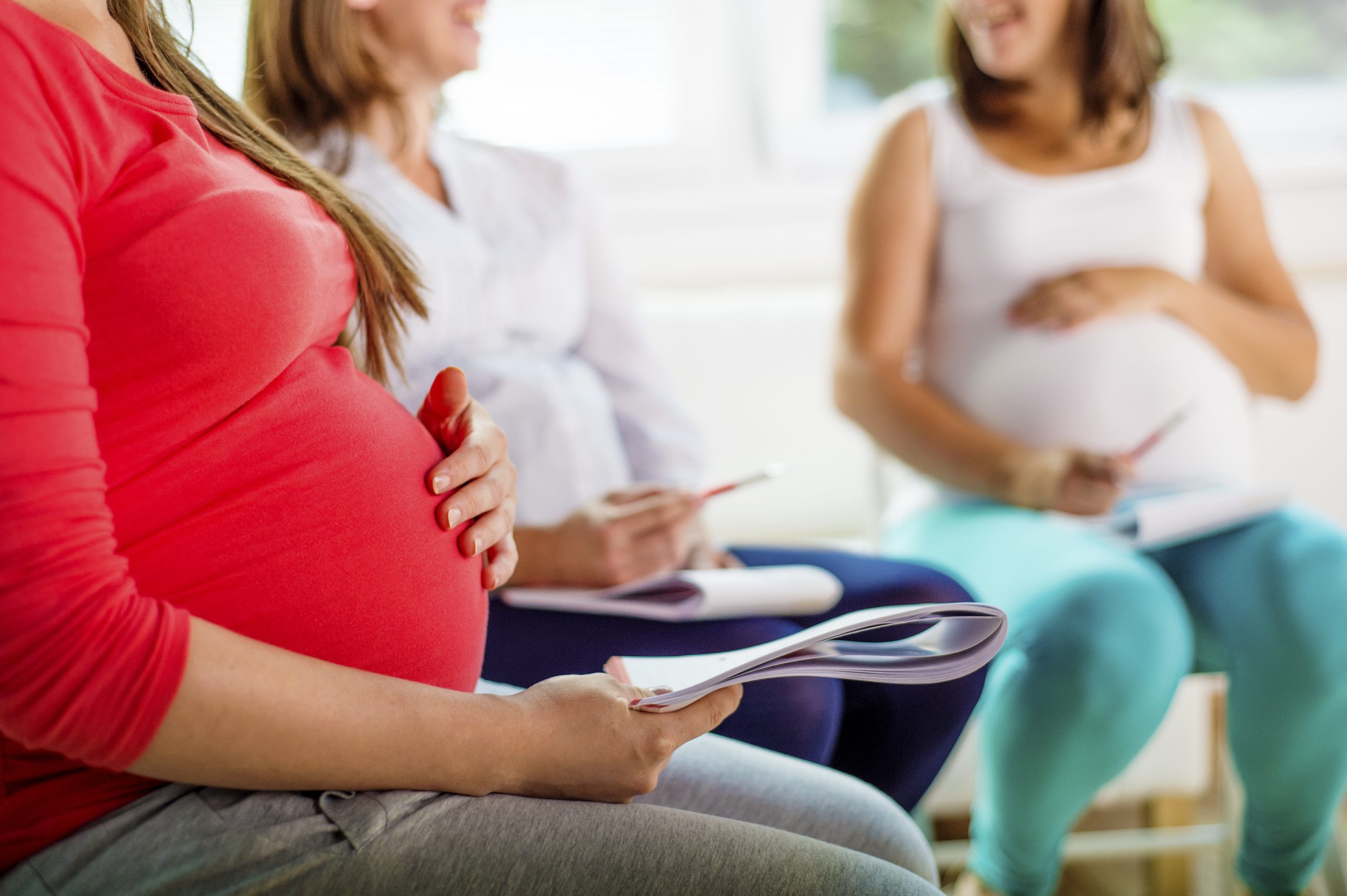 pregnant women sitting in a circle holding bellies during childbirth education class looking at documents and forms and learning about what to expect when you're pregnant