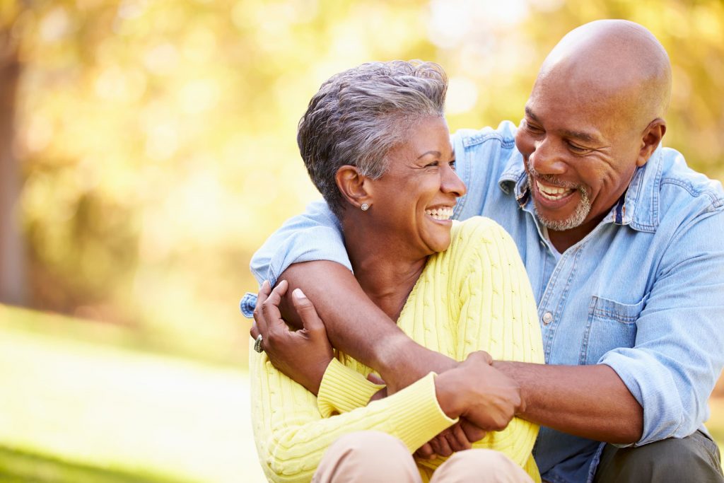 black couple holding each other and smiling while sitting outside in the park