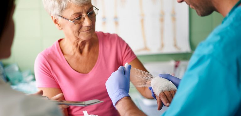 wound care team changing bandage on elderly woman's arm at immediate care
