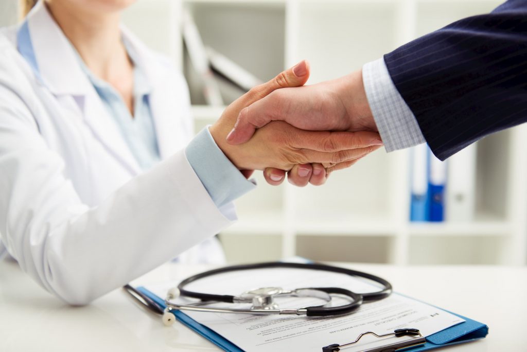 white doctor shaking hands with patient after signing insurance paperwork