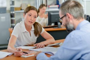 White woman and white man sit at desk going over financial paperwork for good faith estimates and financial assistance to give a good faith estimate or financial assistance