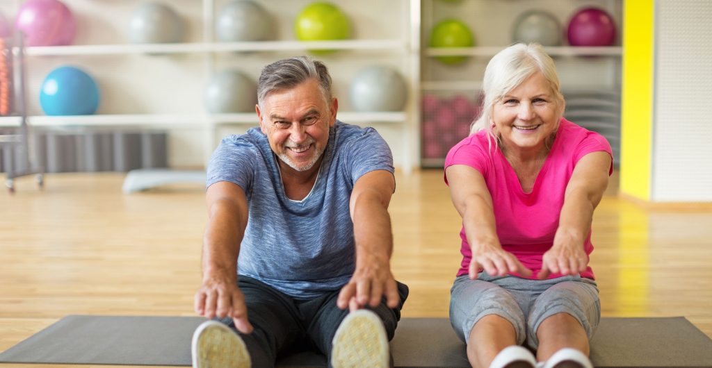 white elderly couple sitting and reaching for toes doing physical therapy and exercising for better health and rehabilitation