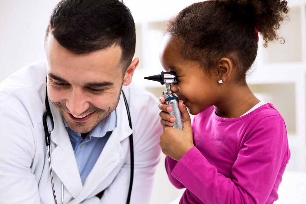 hispanic or white doctor letting black child kid girl looking into his ear with an oscilloscope while smiling at a nmc health locations