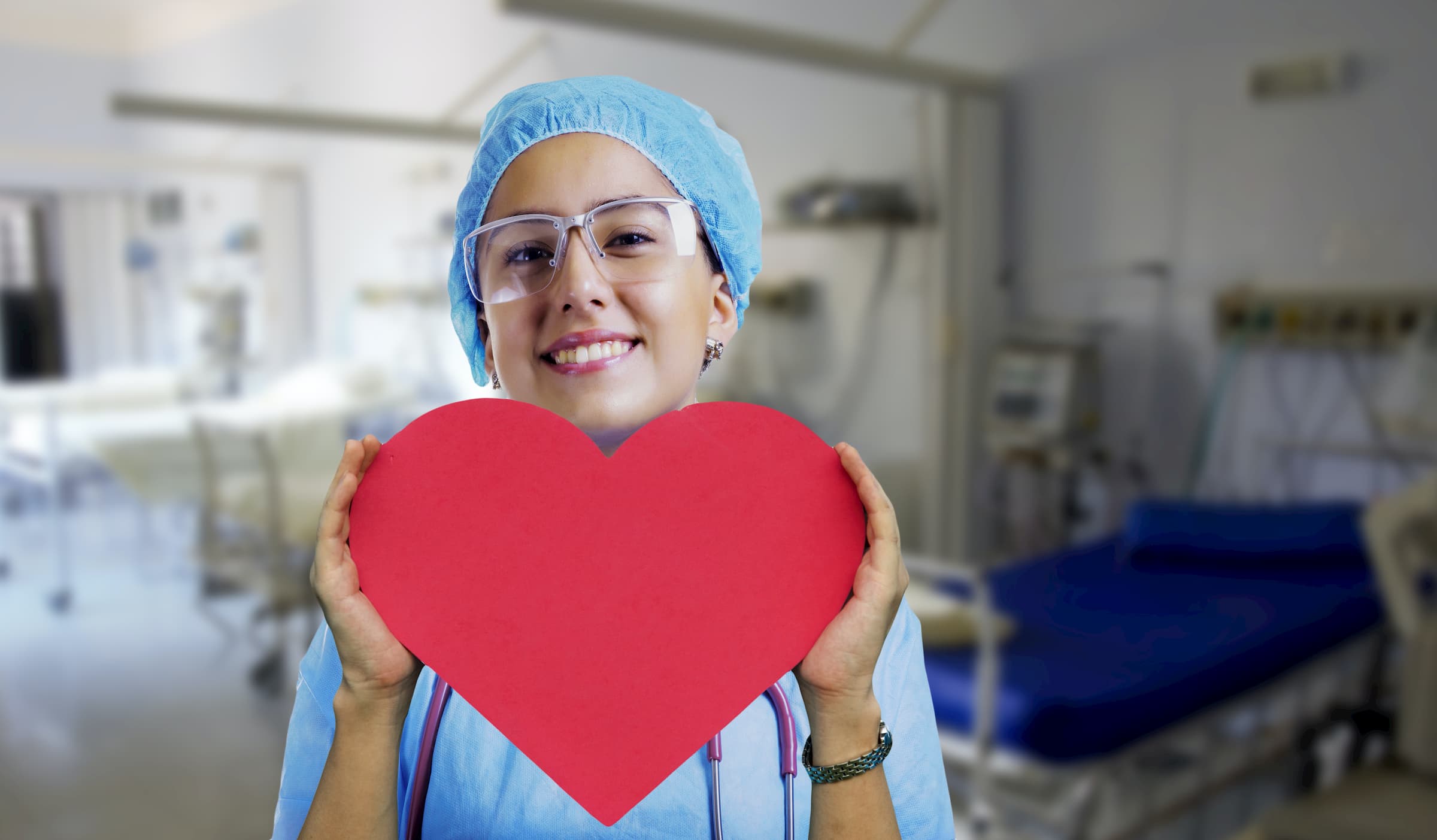 hispanic nurse in blue scrubs and surgical cap holding big red heart in her hands - specialty care