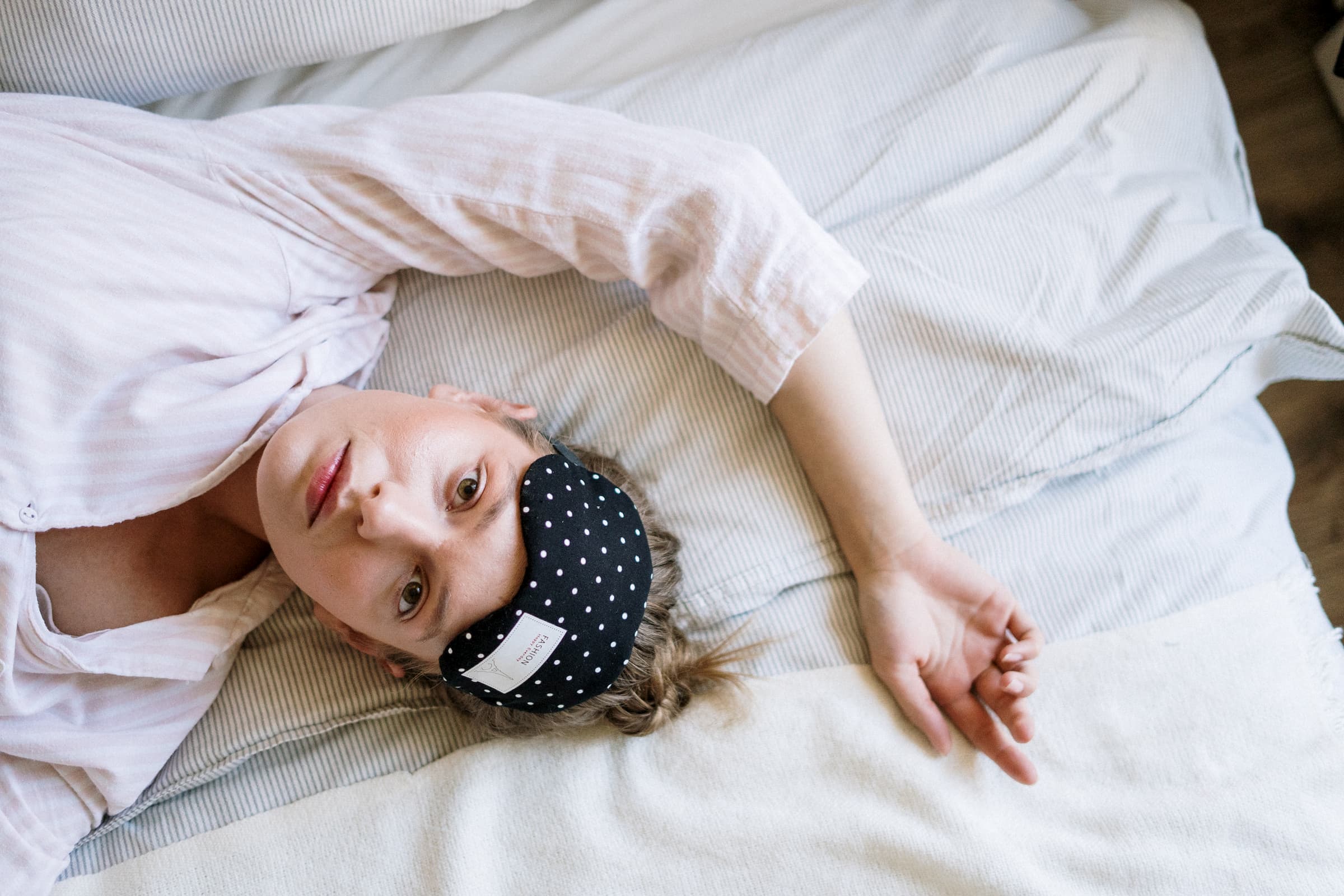 white woman in white shirt laying in bed with sleep mask raised because insomnia can't sleep, sleep disorders, wide awake