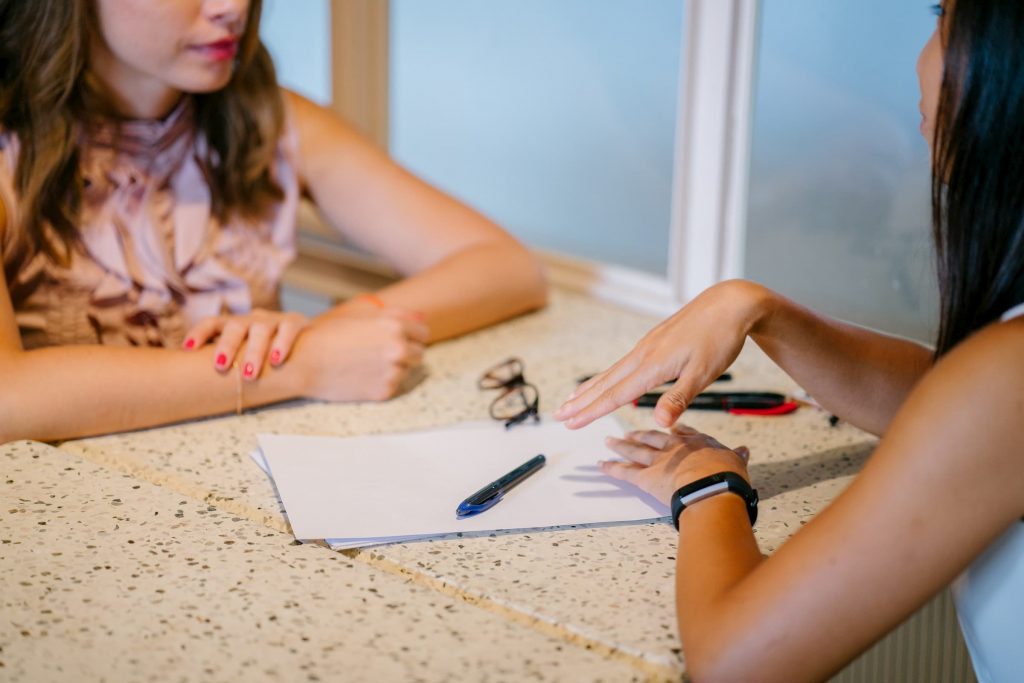 white woman and hispanic woman talking with paper and pen in the middle