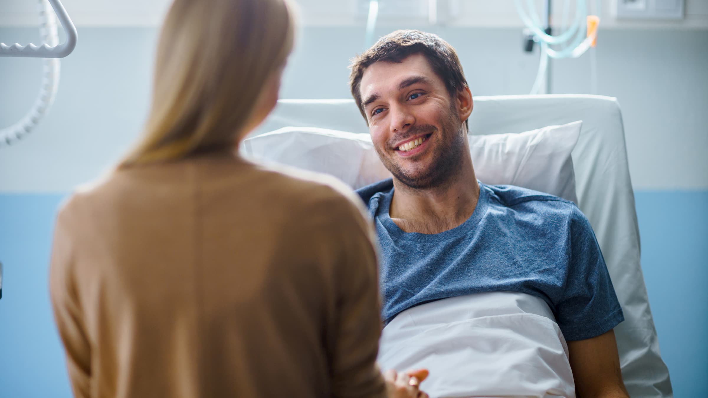 In the Hospital, Man Recovering from Illness Lying in Bed, Loving Wife Visits Him. He is Smiling and Looking at Wife.