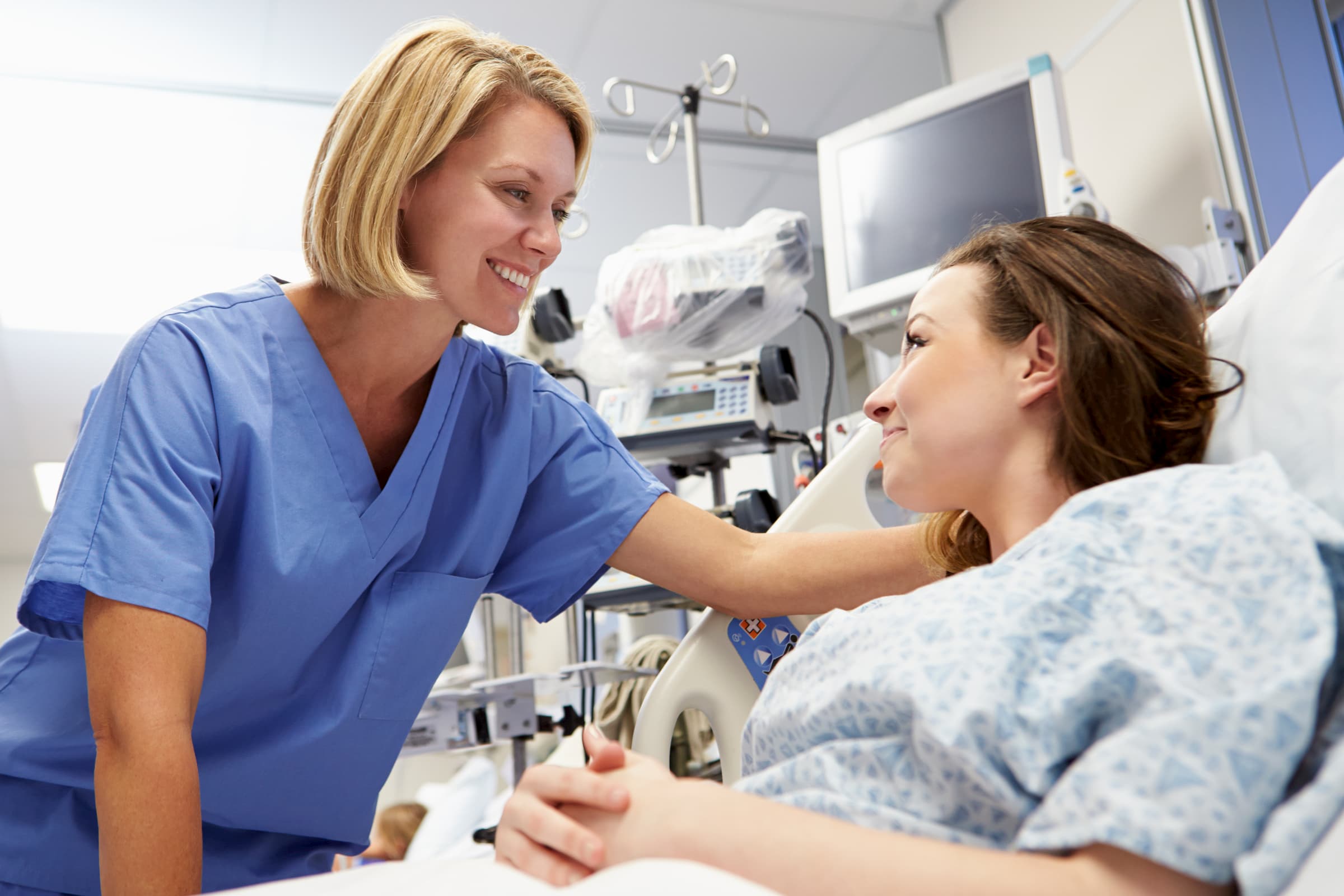 white nurse leaning over white patient in hospital bed inside hospital, stock photo