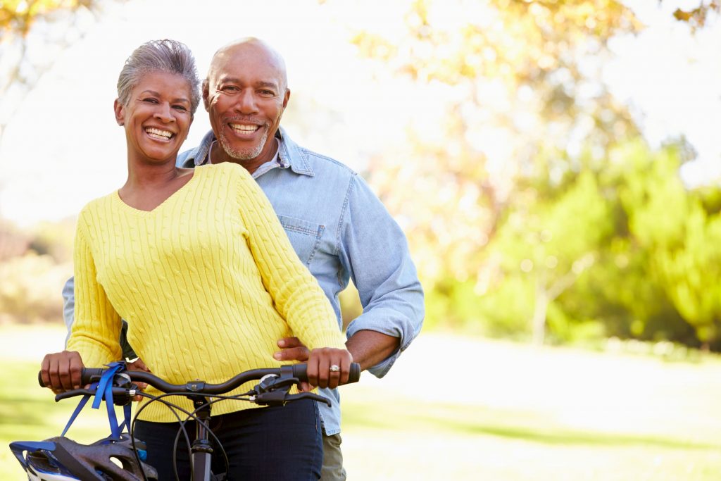 black senior couple in yellow and blue shirt standing outside on bicycle