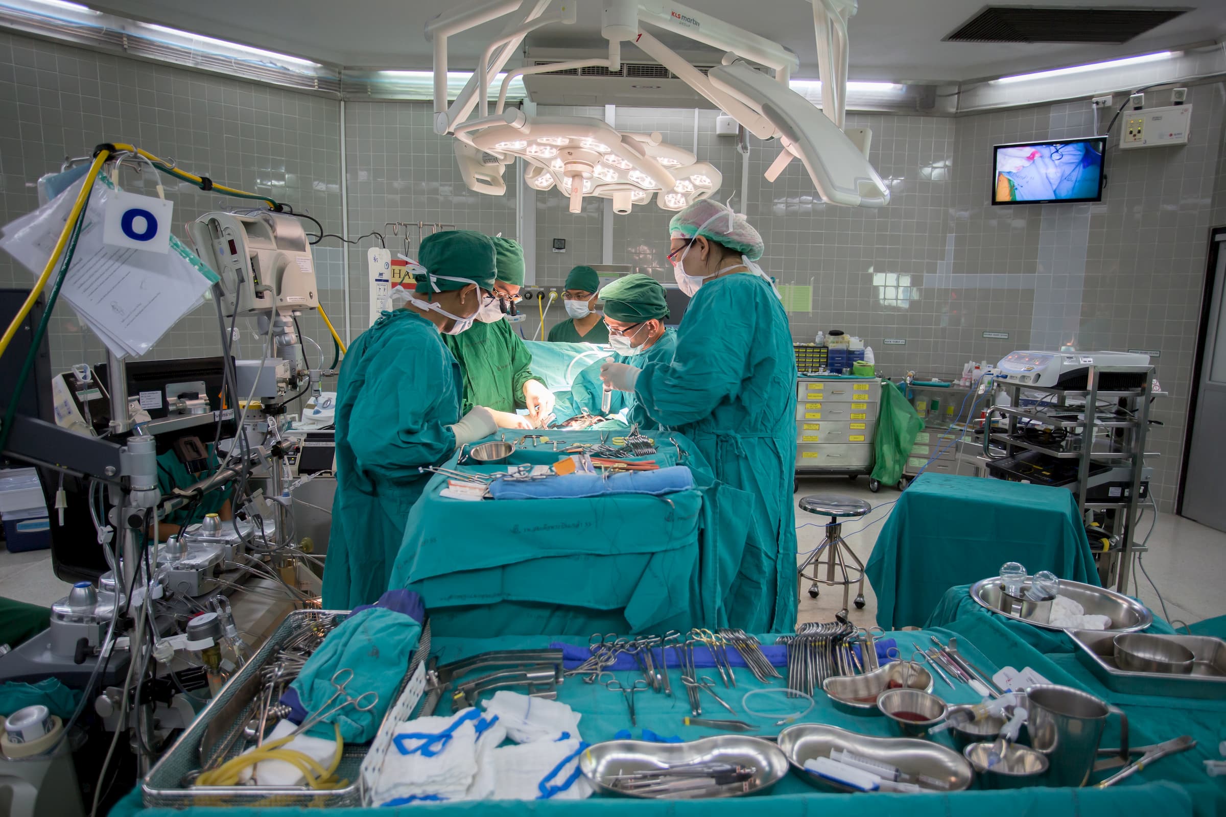 group of doctors inside operating room OR doing surgery on a patient who's on the table in drapes