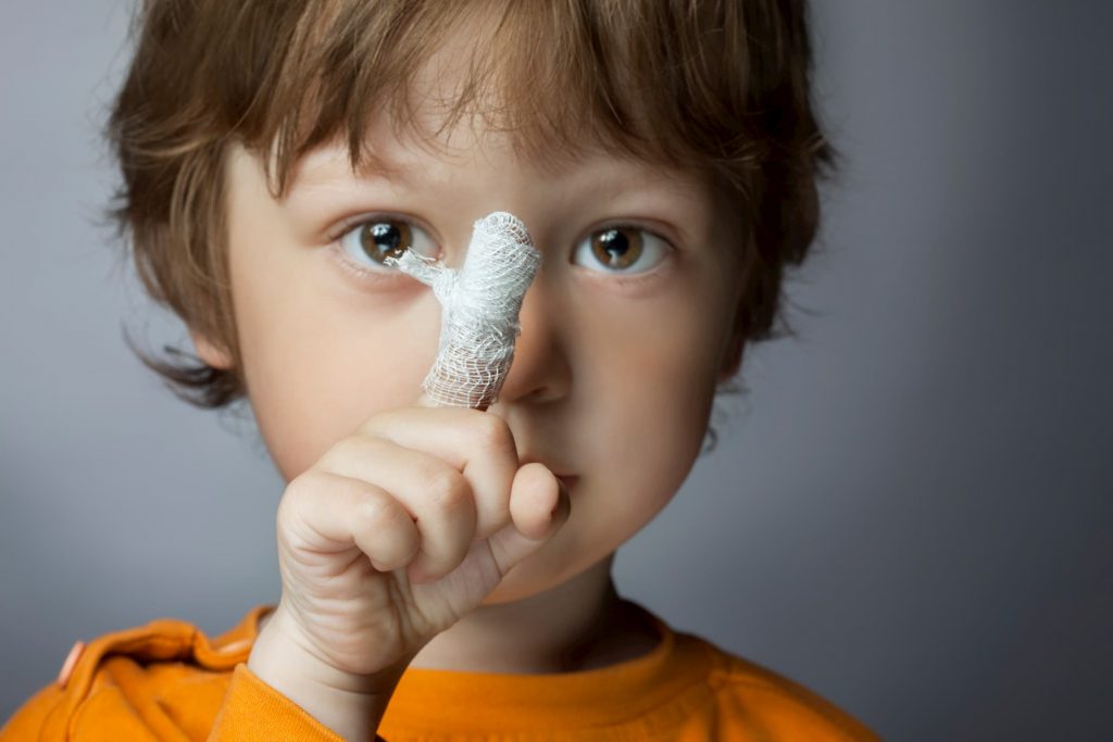 young boy in orange shirt showing pointer finger wrapped in bandage closeup he got at immediate care