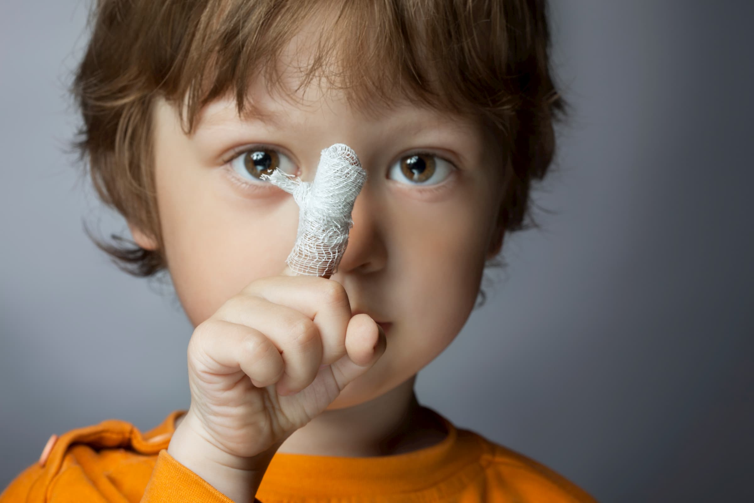 young boy in orange shirt showing pointer finger wrapped in bandage closeup