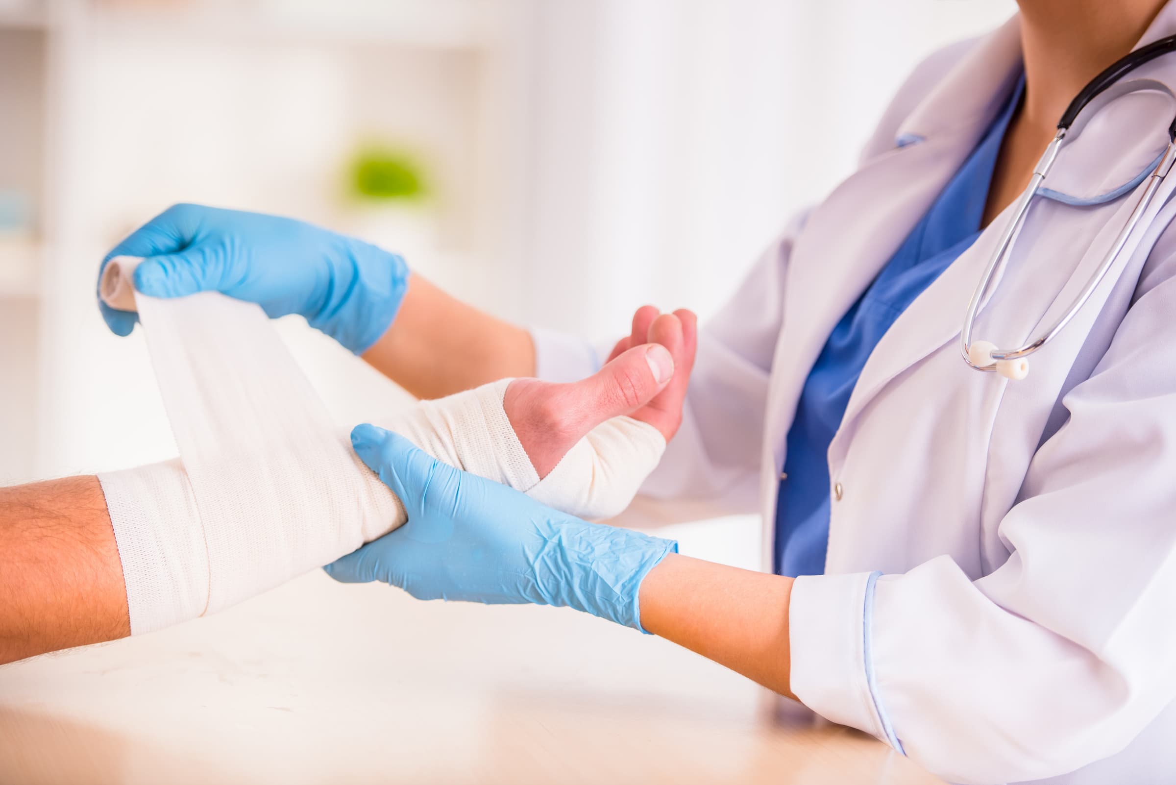 white patient getting hand wrapped by why doctor wearing blue surgical gloves