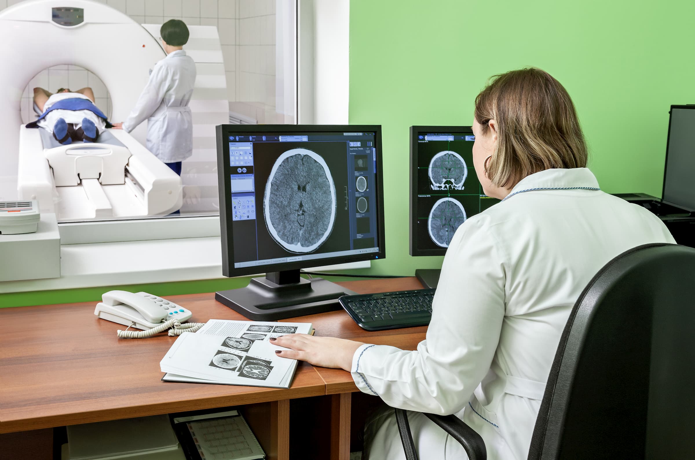 white female doctor looking at brain scan while person gets brain scan in other room
