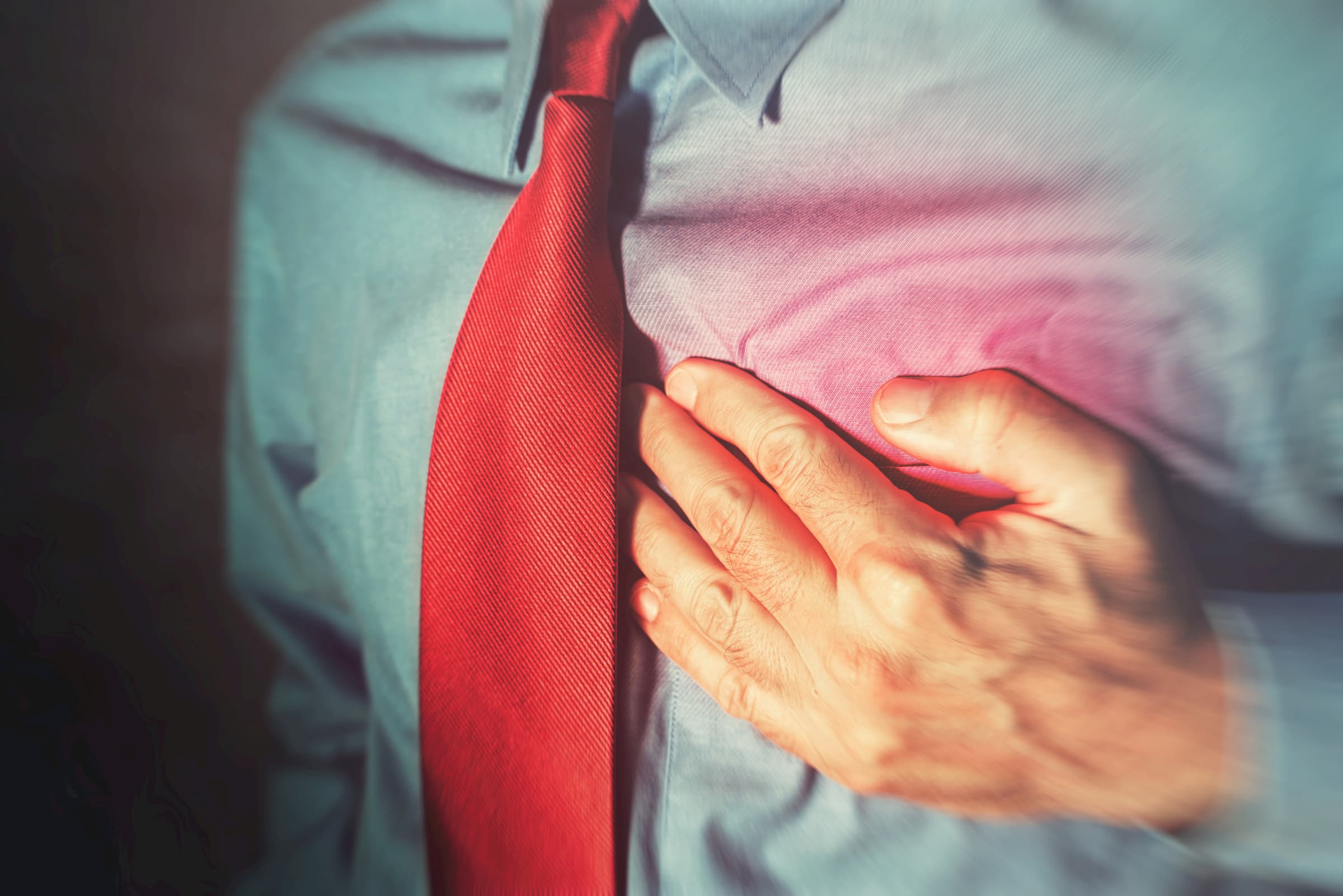 man in blue dress shirt with red tie clenching chest showing heart attack