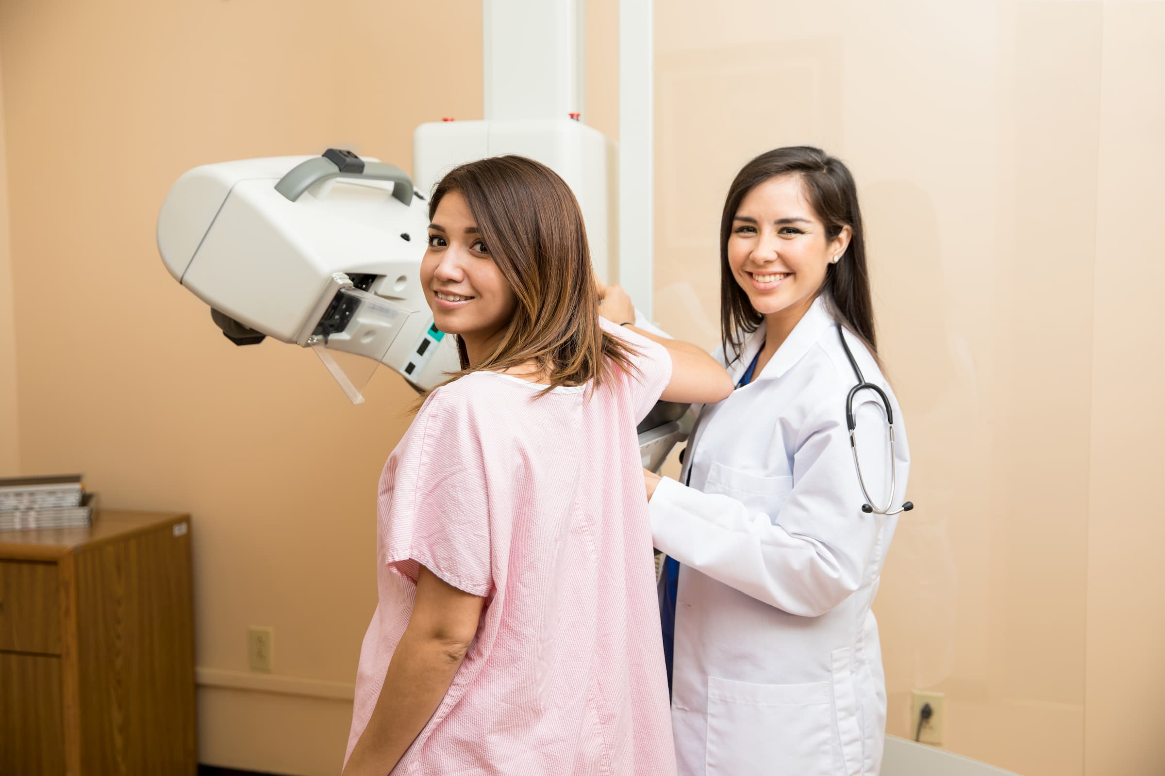 hispanic woman getting mammogram with hispanic doctor standing beside 3d mammography machine smiling