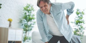 senior white man bent over in pain because of back pain with grimace on face