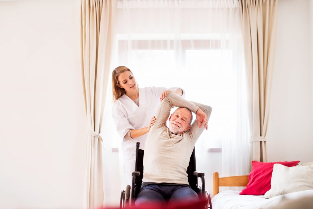 white nurse helping white senior man stretch during inpatient rehab while in wheelchair in patient room at hospital facility