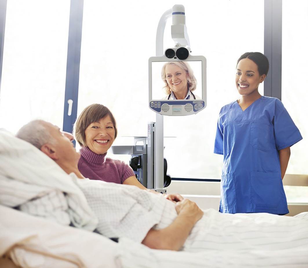 white man lying in hospital bed talking on telemedicine appointemnt with doctor white wife sitting next to him, smiling and black nurse smiling next to bed