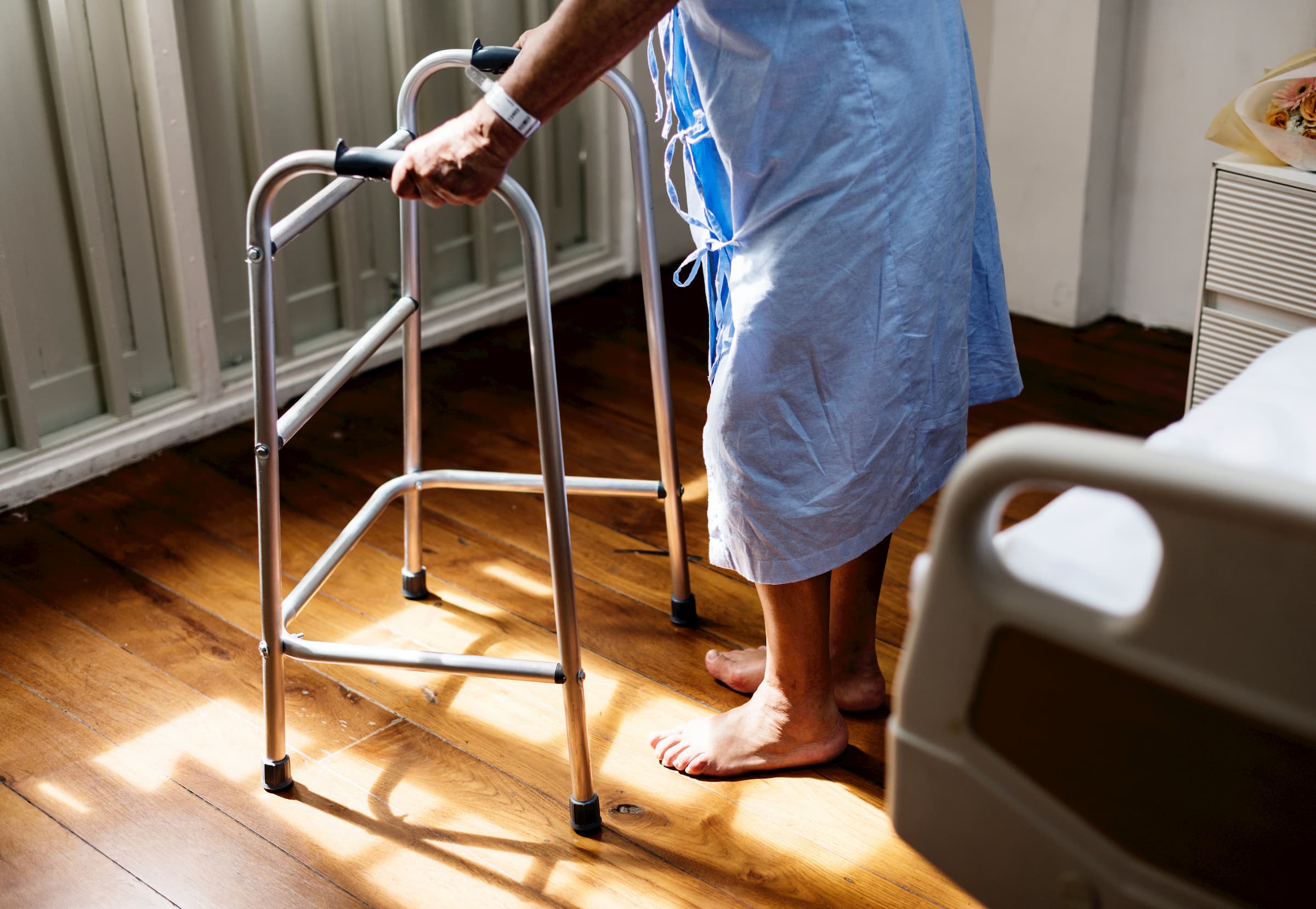 older senior man walking with walker in hospital gown in hospital room - stock image