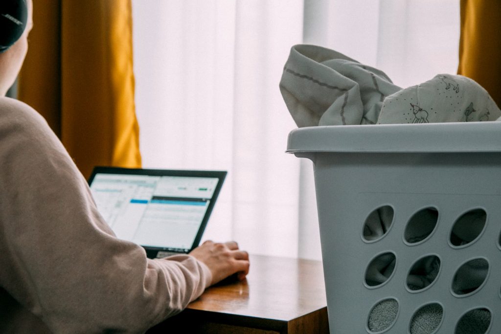 woman on computer with basket of unfolded laundry next to her