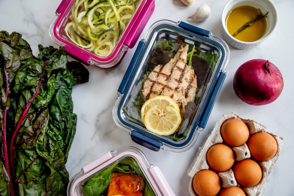 shot of meal prepped meat and veggies and eggs and fruit on white background sitting on table