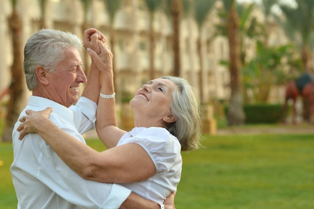 senior white man and woman in white shirts dancing outside on vacation