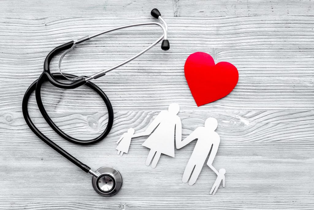 gray background with black stethoscope, white paper family with child female woman male man and another child and heart above them to show community health needs assessment; stock photo