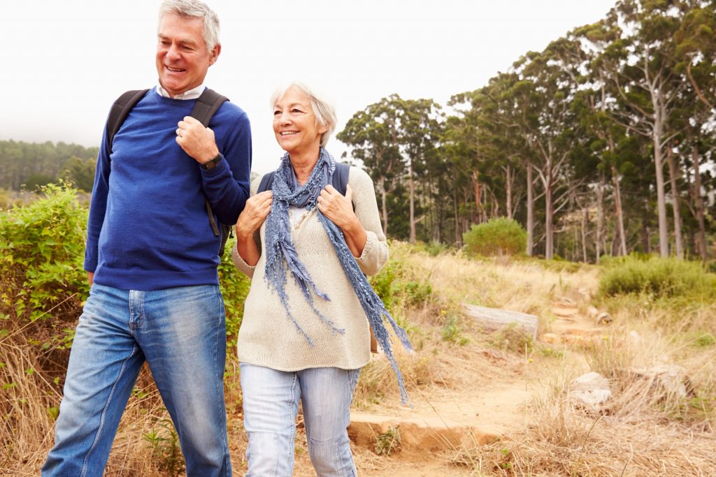 man in blue sweater and jeans, woman in cream sweater and blue scarf and jeans hiking on a trail