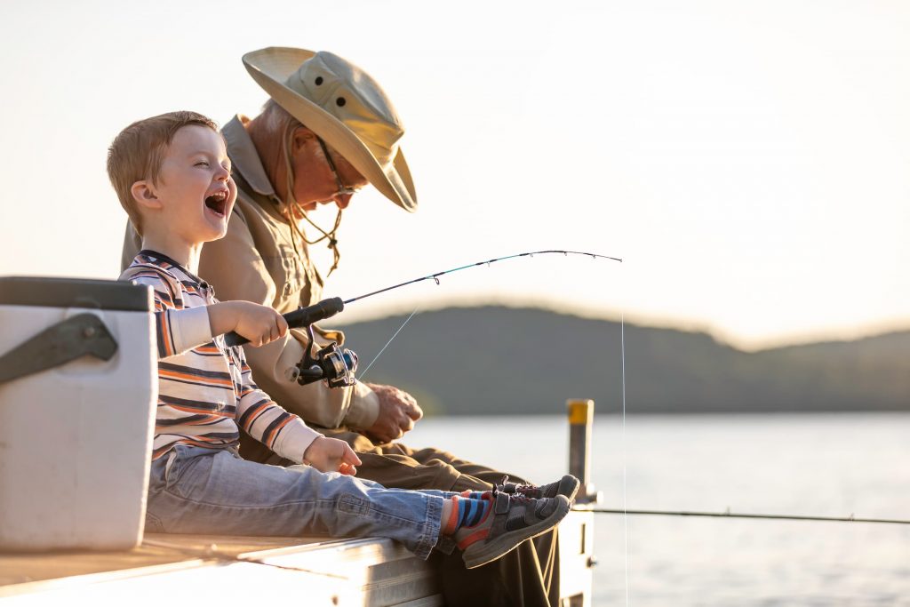 young boy and grandpa fishing off a dock with fishing poles and cooler and tackle box