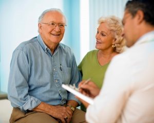 senior white couple sitting in doctor's office with male doctor in white lab coat not facing the camera