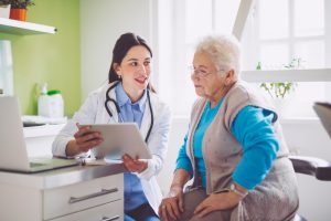 doctor explaining health forms insurance information financial assistance and health ethics to senior elderly patient in doctor's office viewing patient resources and patient education