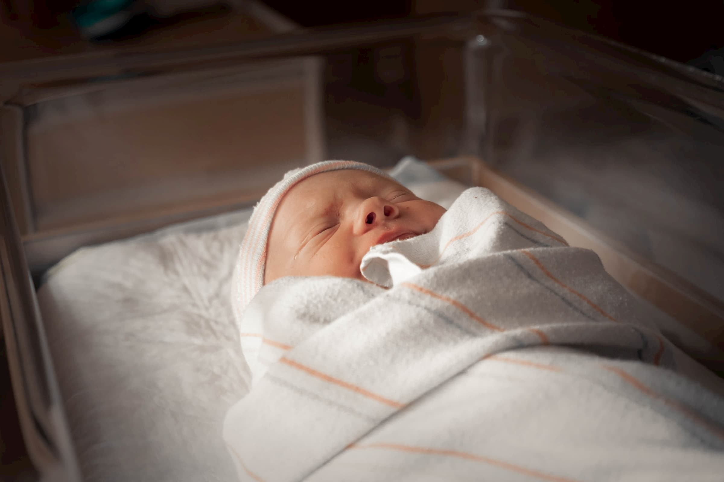 small newborn baby swaddled in blanket and hat in special care nursery stock photo