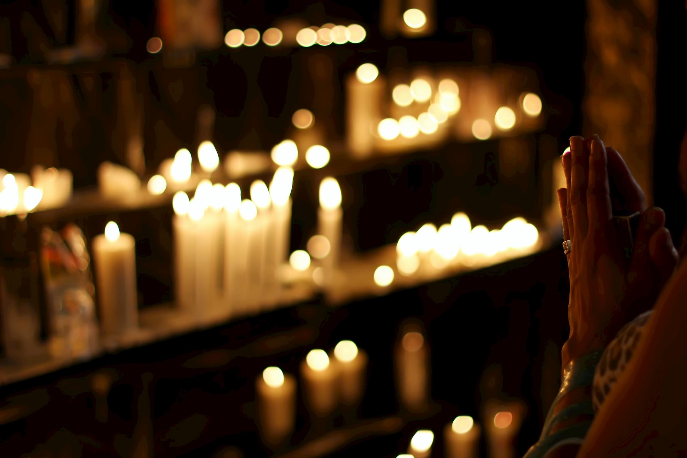 blurred out dark photo of candlelight candle altar and woman praying with prayer hands in the dark