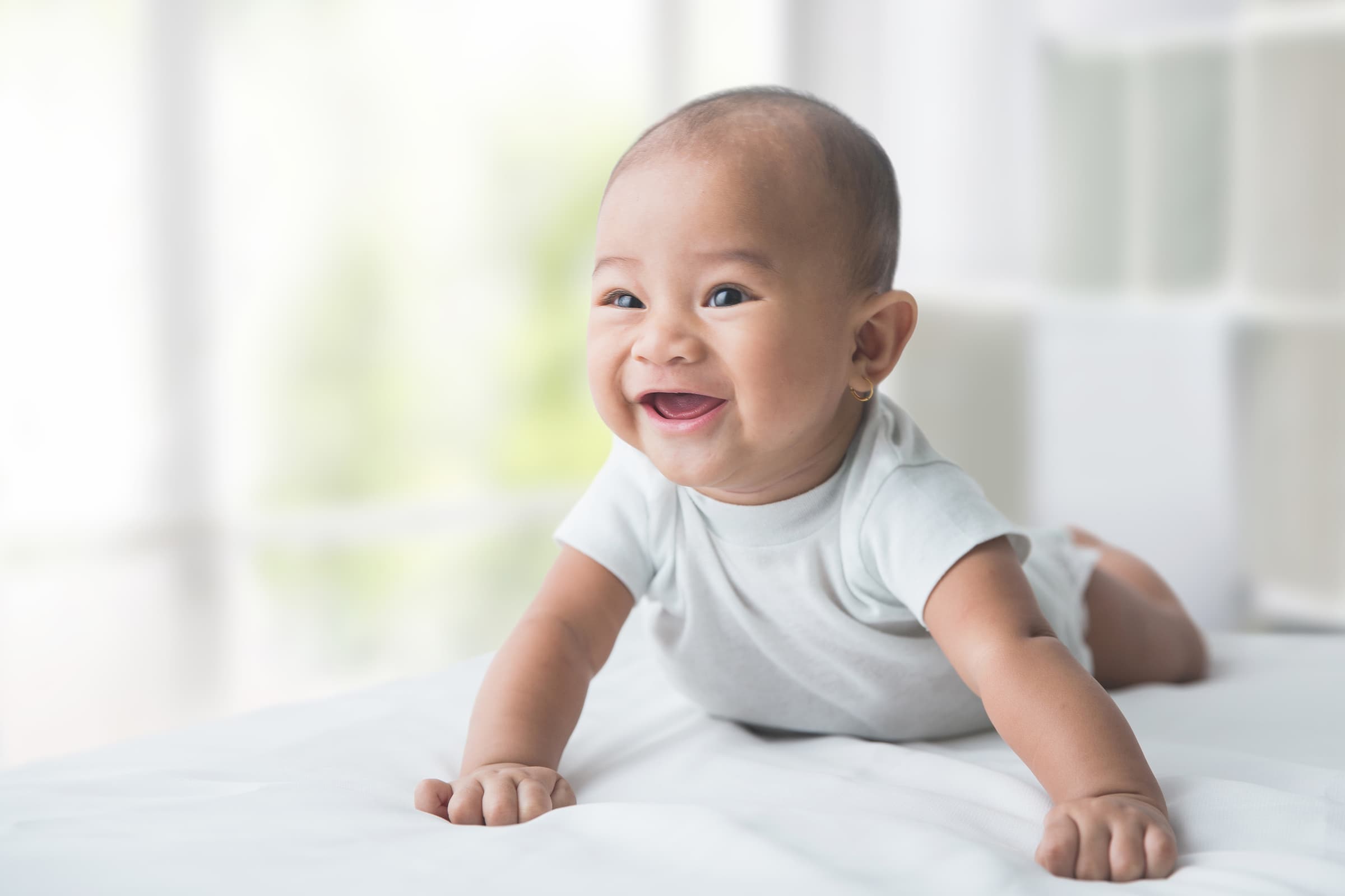 smiling happy baby while tummy time at home, asian