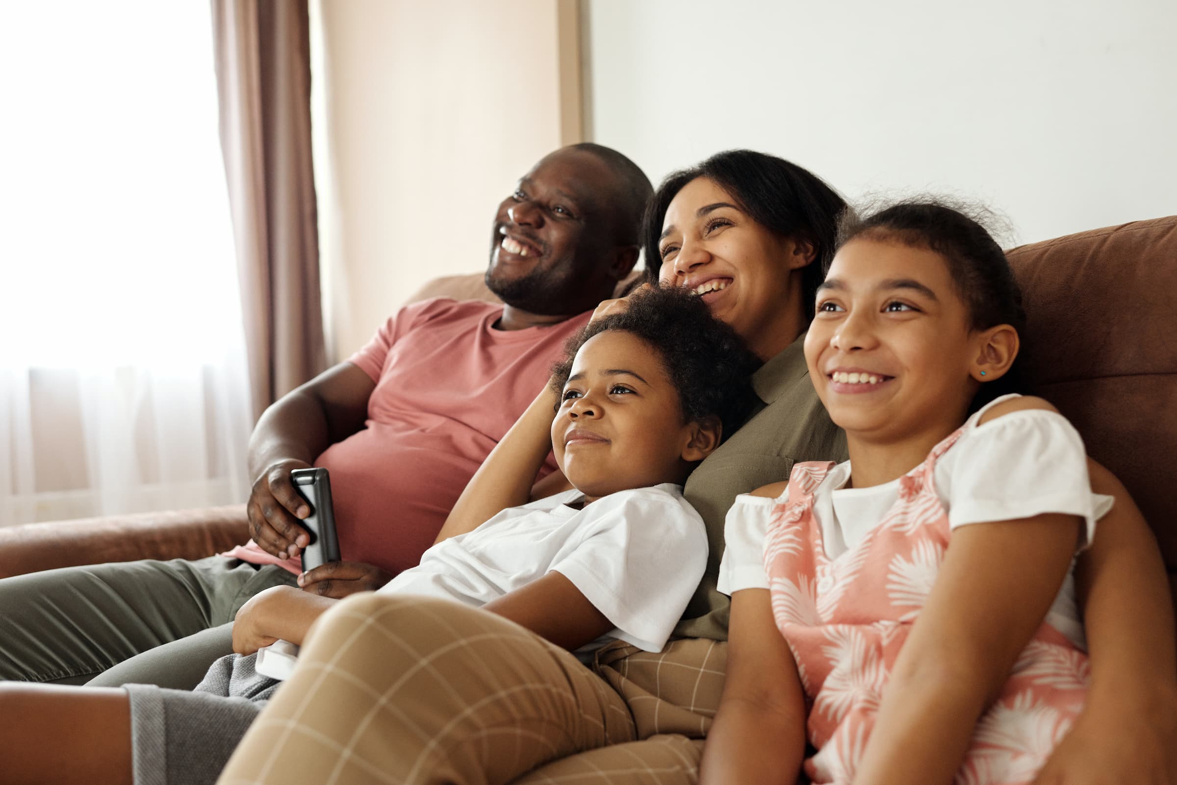 black hispanic family sitting on couch looking at tv television off into the distance watching super bowl game