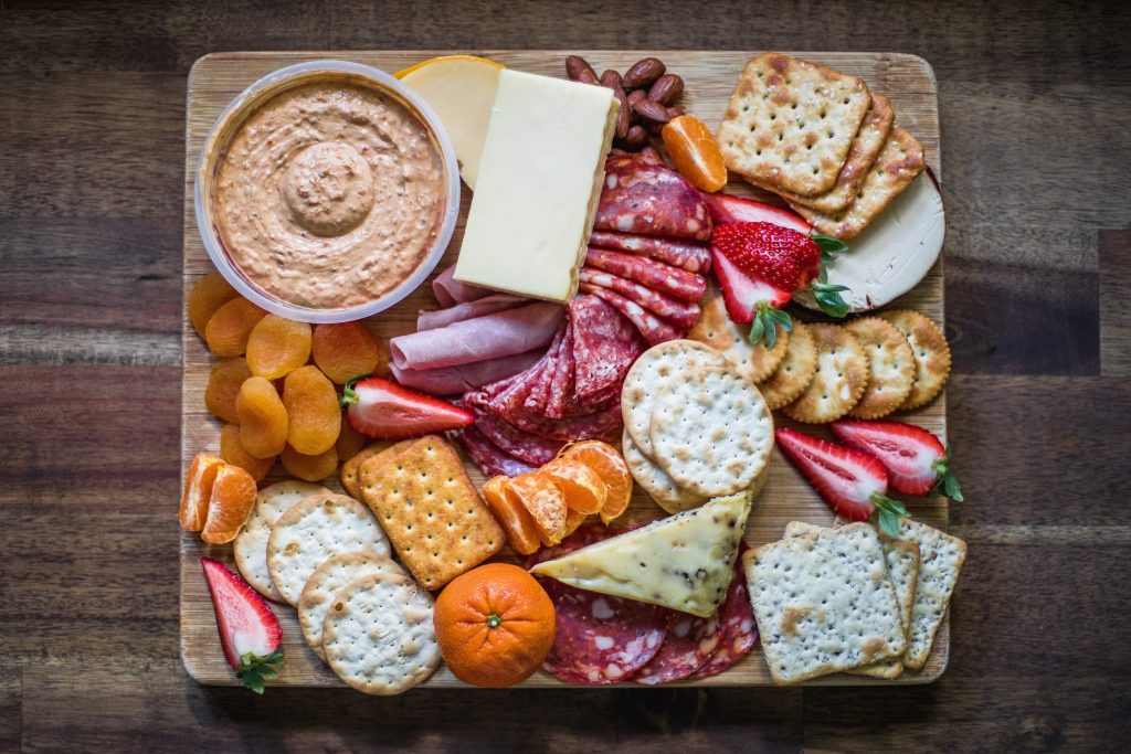 birds eye photo of cheese platter with hummus, crackers, different cheeses and healthy snacks for super bowl party