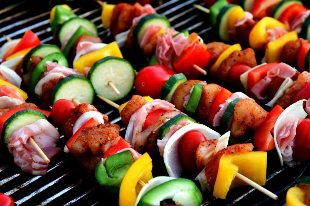 Up close shish kabobs with cucumbers, tomatoes, shrimp, chicken, bacon, yellow peppers, green peppers, onions and red peppers