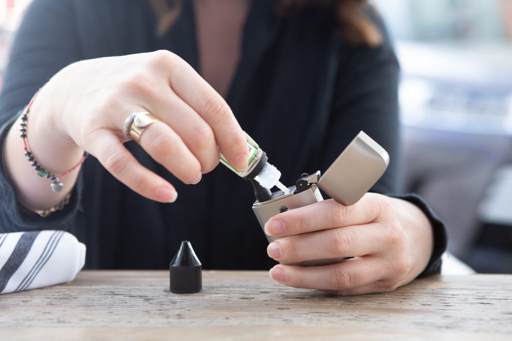 young adult woman filling vape mod e-cigarette with vape juice